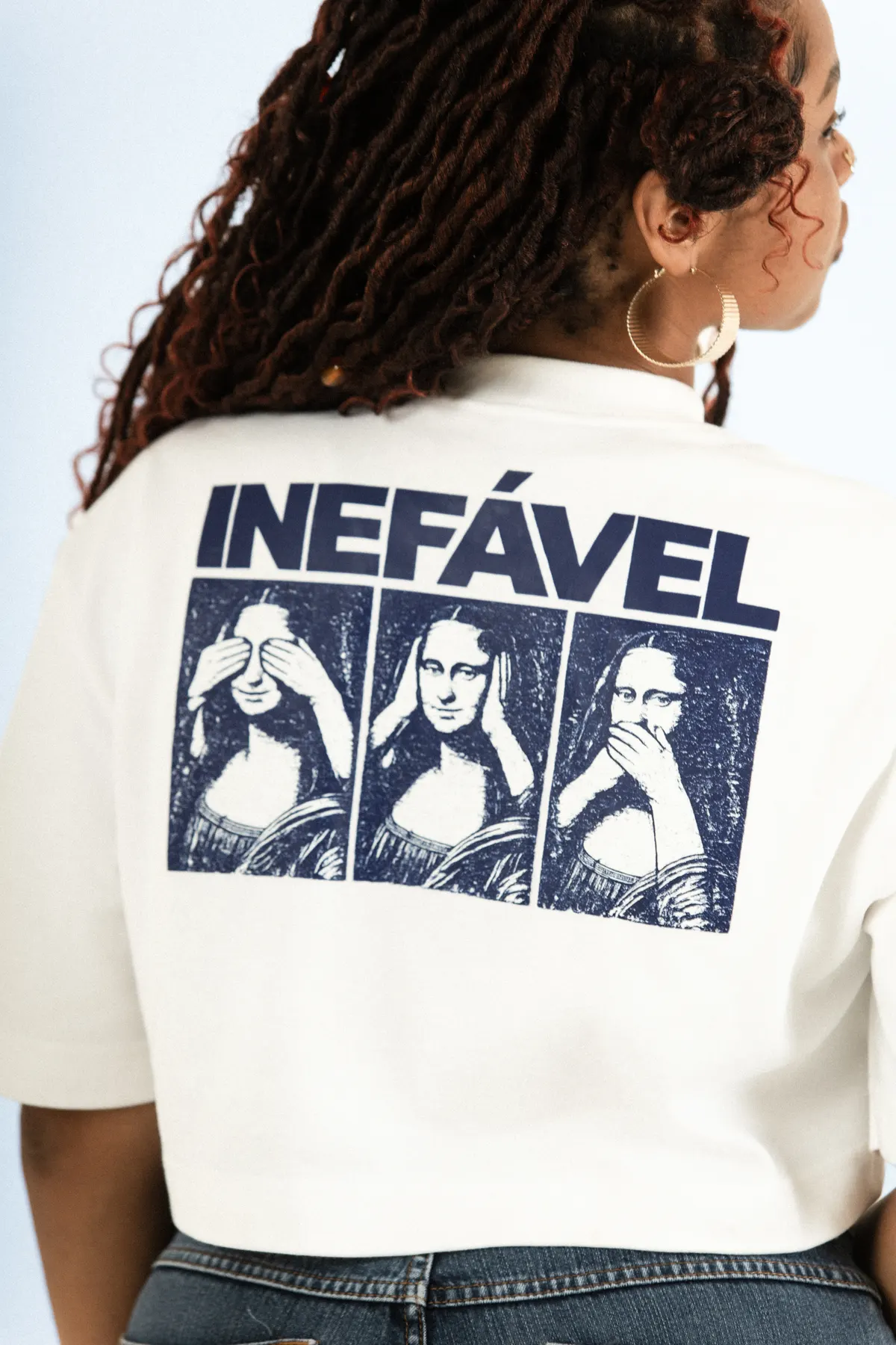 Modelo de costas, com o cropped branco e a estampa Inefável de três rostos azuis.