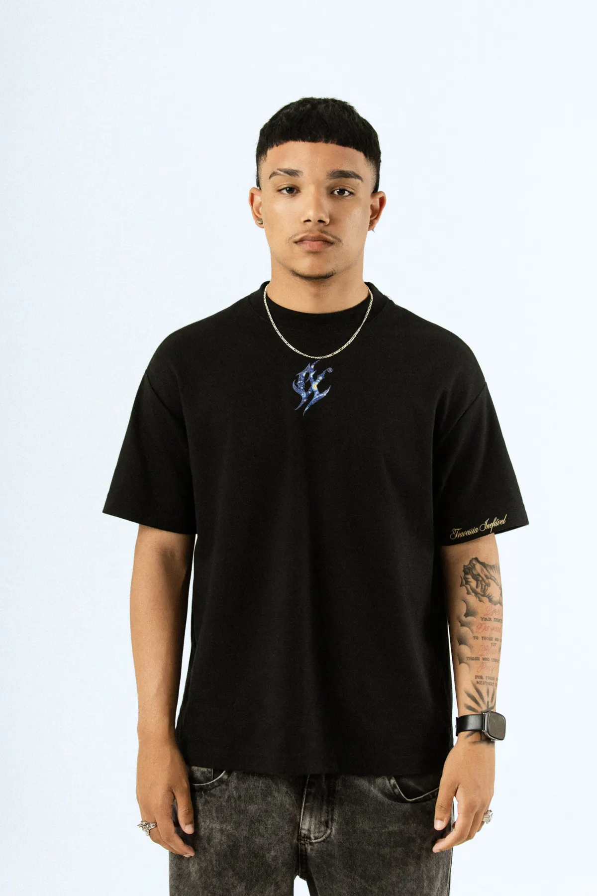 Modelo de corrente fina, de frente, com a camiseta preta e a marca azul bordada no peito.
