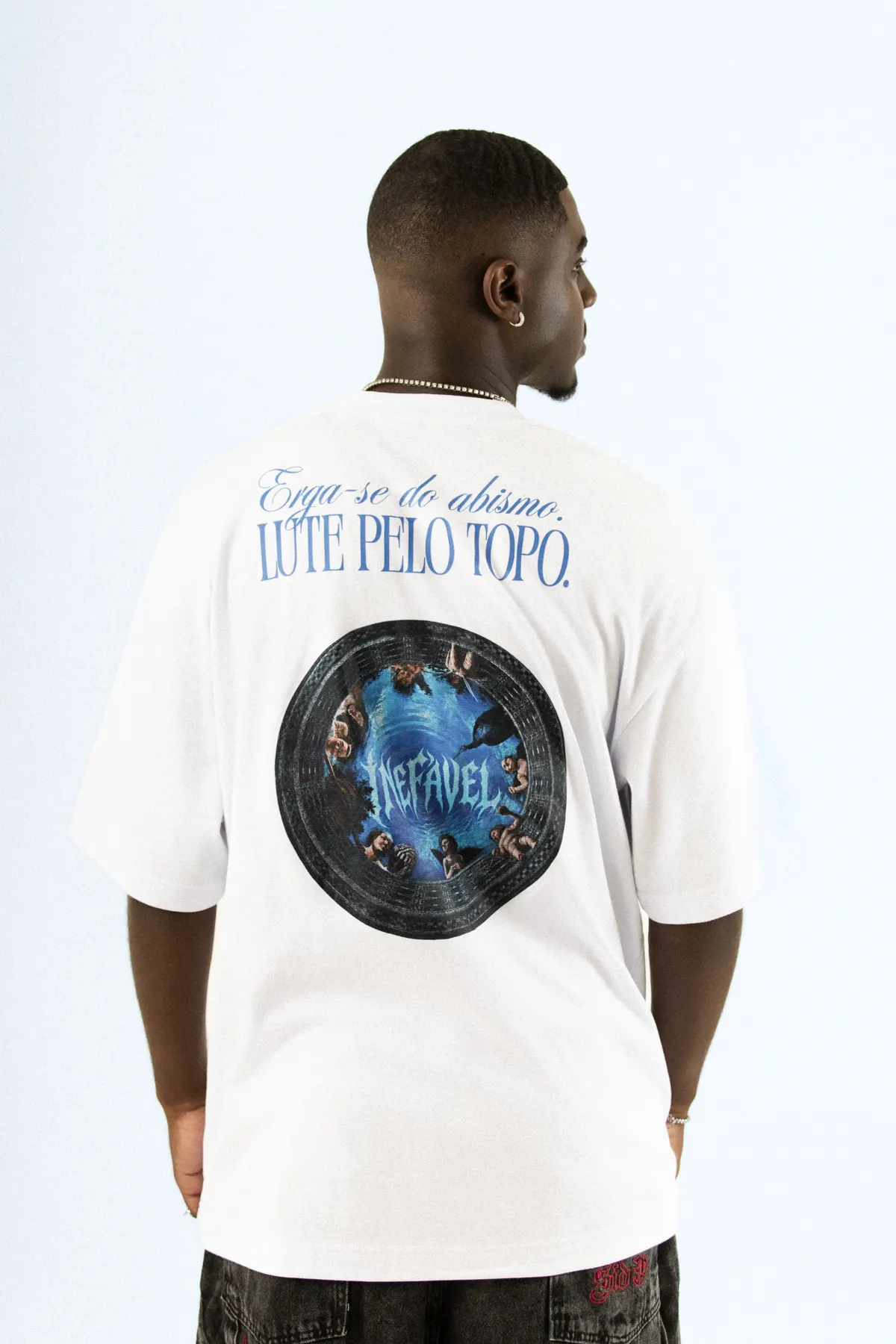 Modelo de costas, com a camiseta branca e a estampa circular Inefável sob a frase Lute pelo topo.